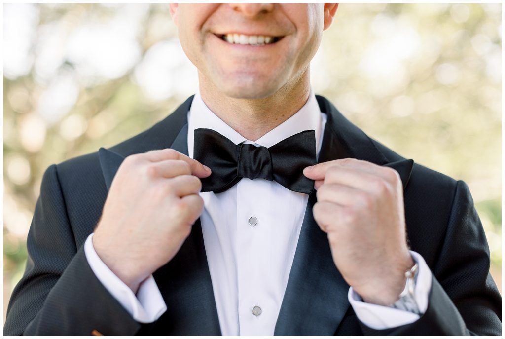 Smiling groom holding onto his black bowtie