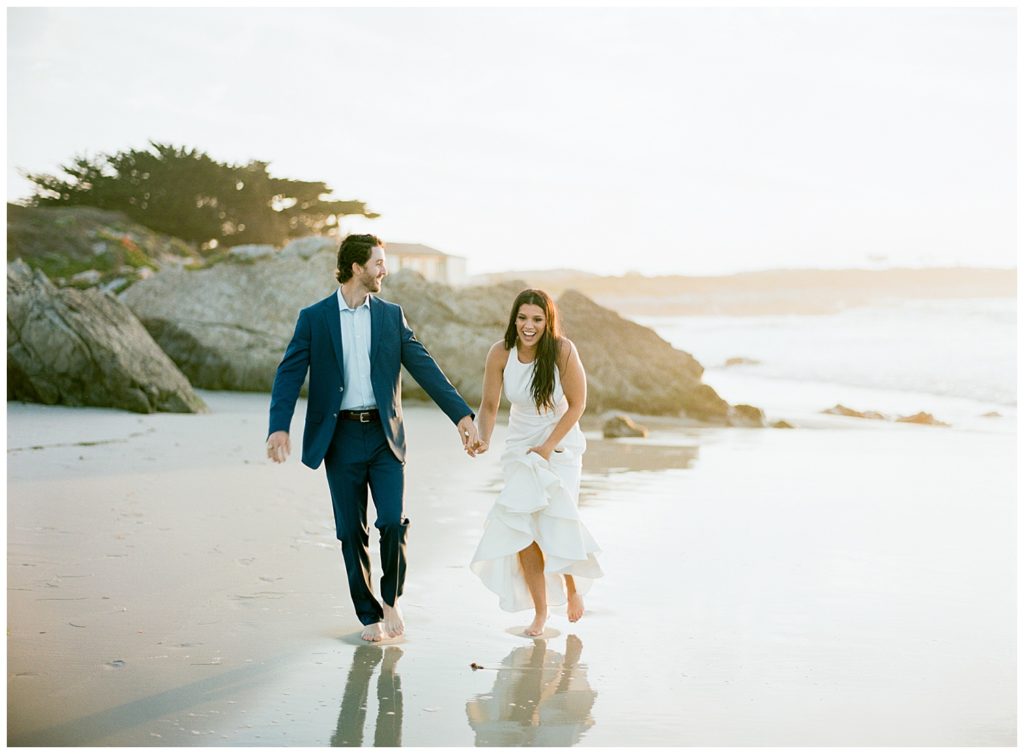 couple holding hands and running on the Pebble Beach shoreline