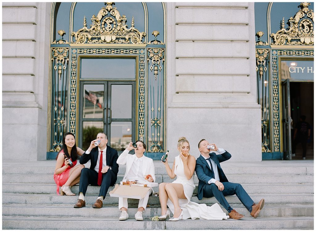 photo of the brides and their friends on the steps of San Francisco City Hall enjoying pizza and champagne by film photographer AGS Photo Art