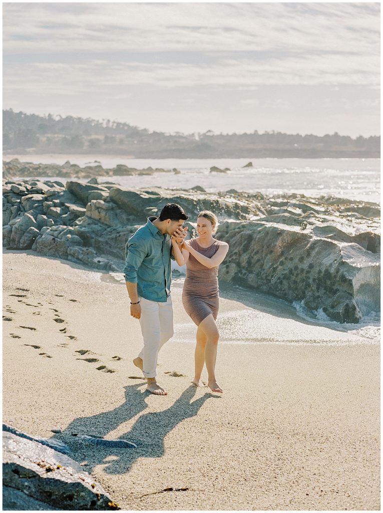 portrait of a newly engaged couple walking hand in hand along the beach