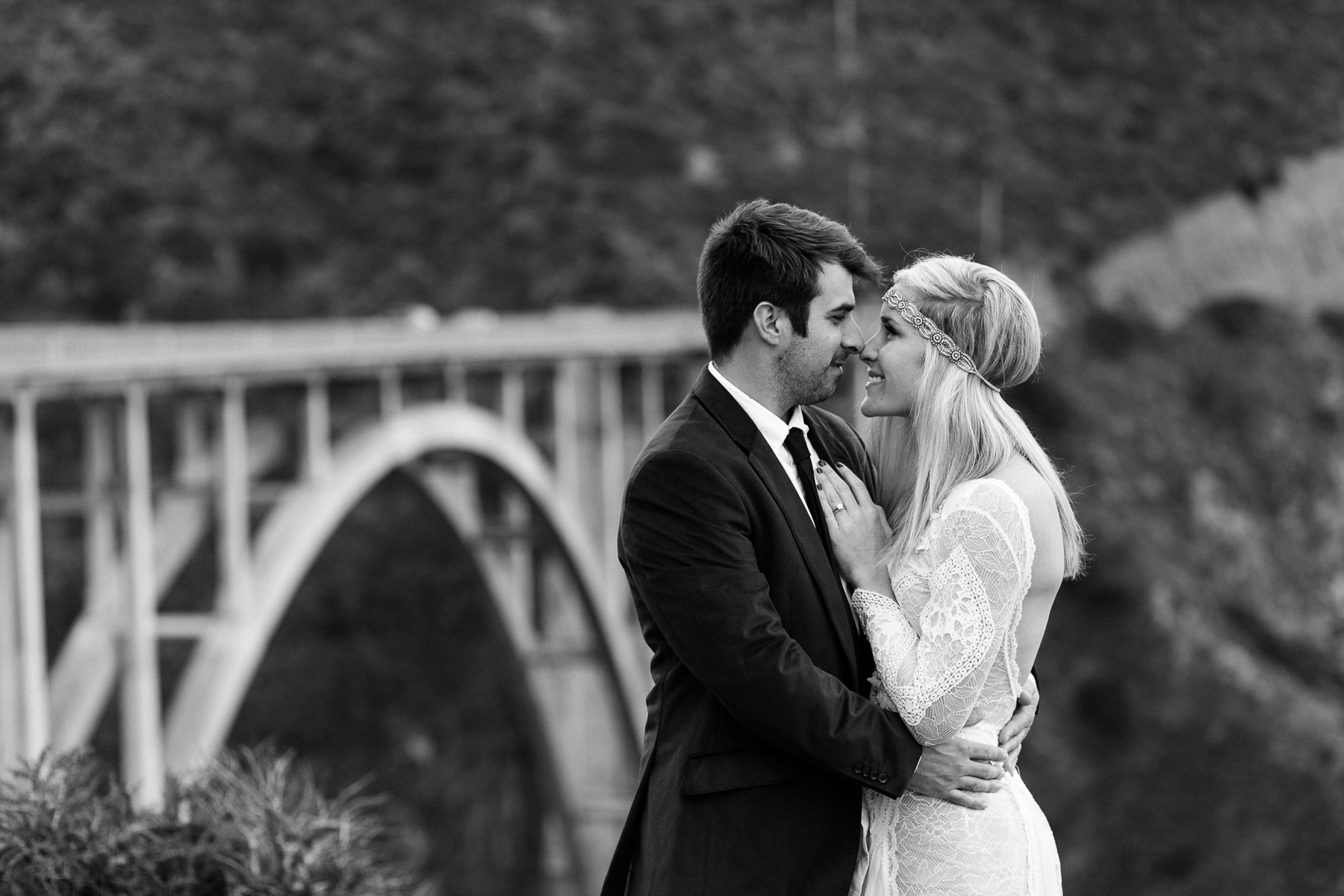Boho bride embraces her groom in front of Bixby Bridge in Big Sur