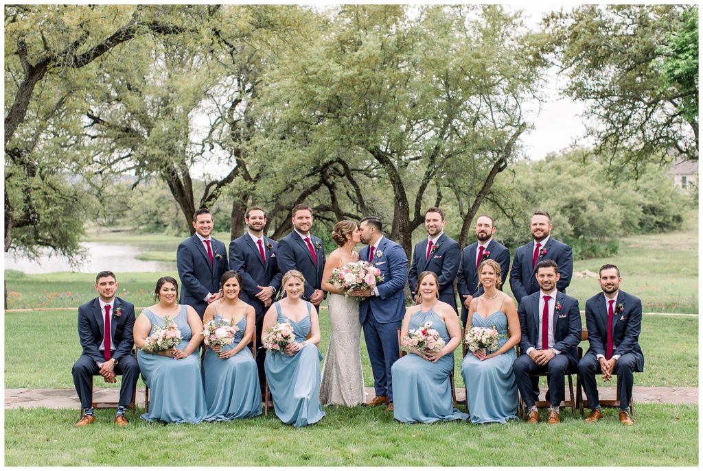 Full bridal party portrait with bride and groom kissing in middle at Ma Maison