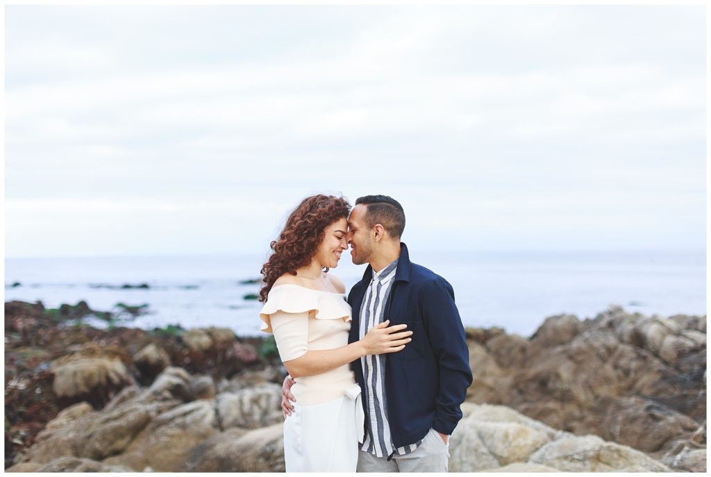 Couple embracing one another with rocky cliffs and the ocean behind them