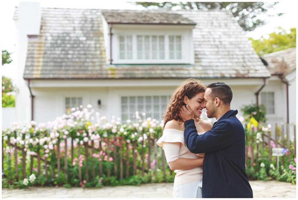 couple embracing in front of a vintage house and flower fence