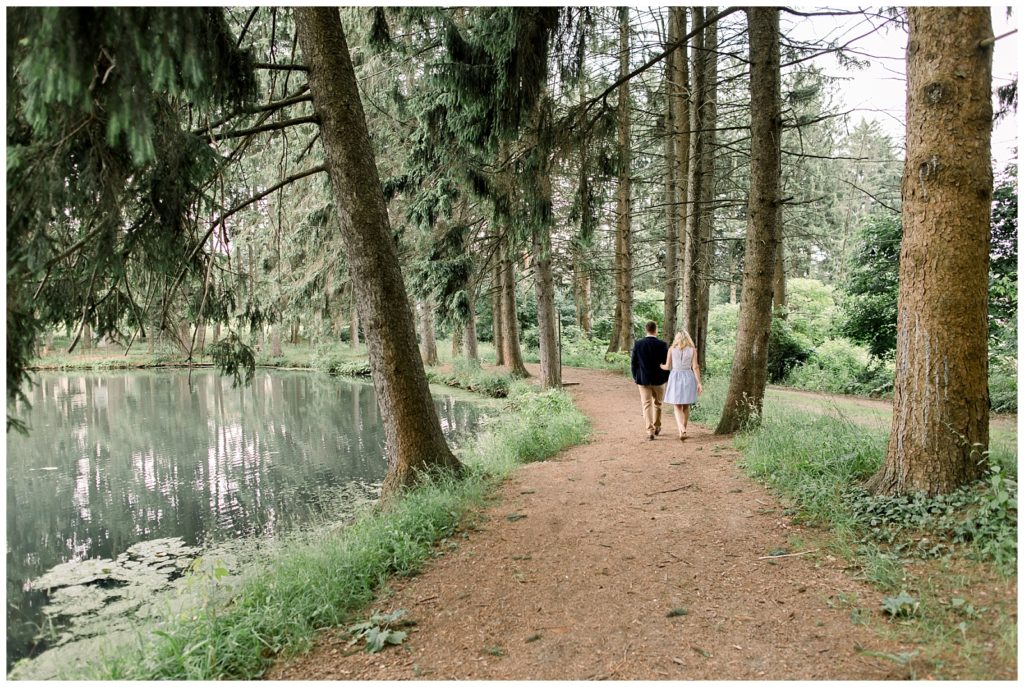 forest shot of couple walking down a trail surrounded by trees and a lake