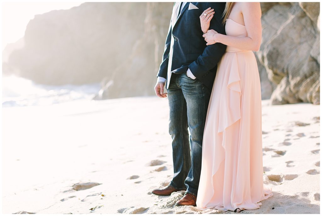 formalwear couple in pastel pink flowy dress and navy blue sports coat on the beach overlooking the ocean from the coastline