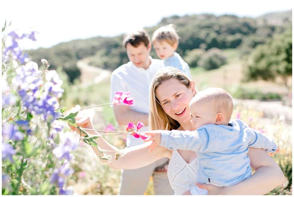 Family portrait with mother holding her baby reaching out to pink and purple flowers while father holds their son