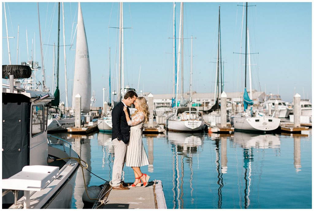 Engagement photograph of Carmel couple standing on the docks with their foreheads touching and many boats in the background by film photographer Ags Photo Art