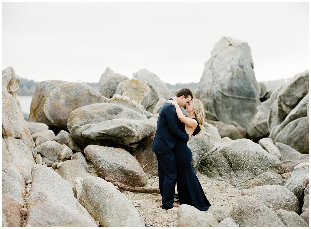 navy blue suit and dress couple embracing on the rocks at Carmel Beach by film photographer AGS Photo Art