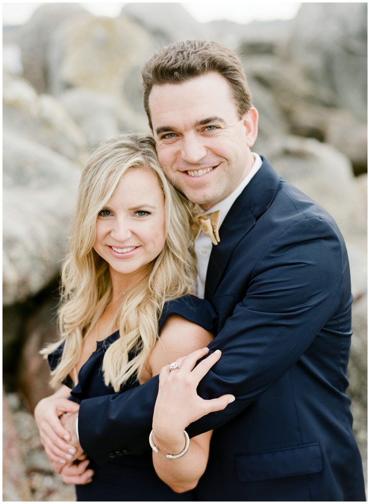 portrait on the rocks at Carmel Beach of Monterey couple in a deep navy blue suit and gown by film photographer AGS Photo Art