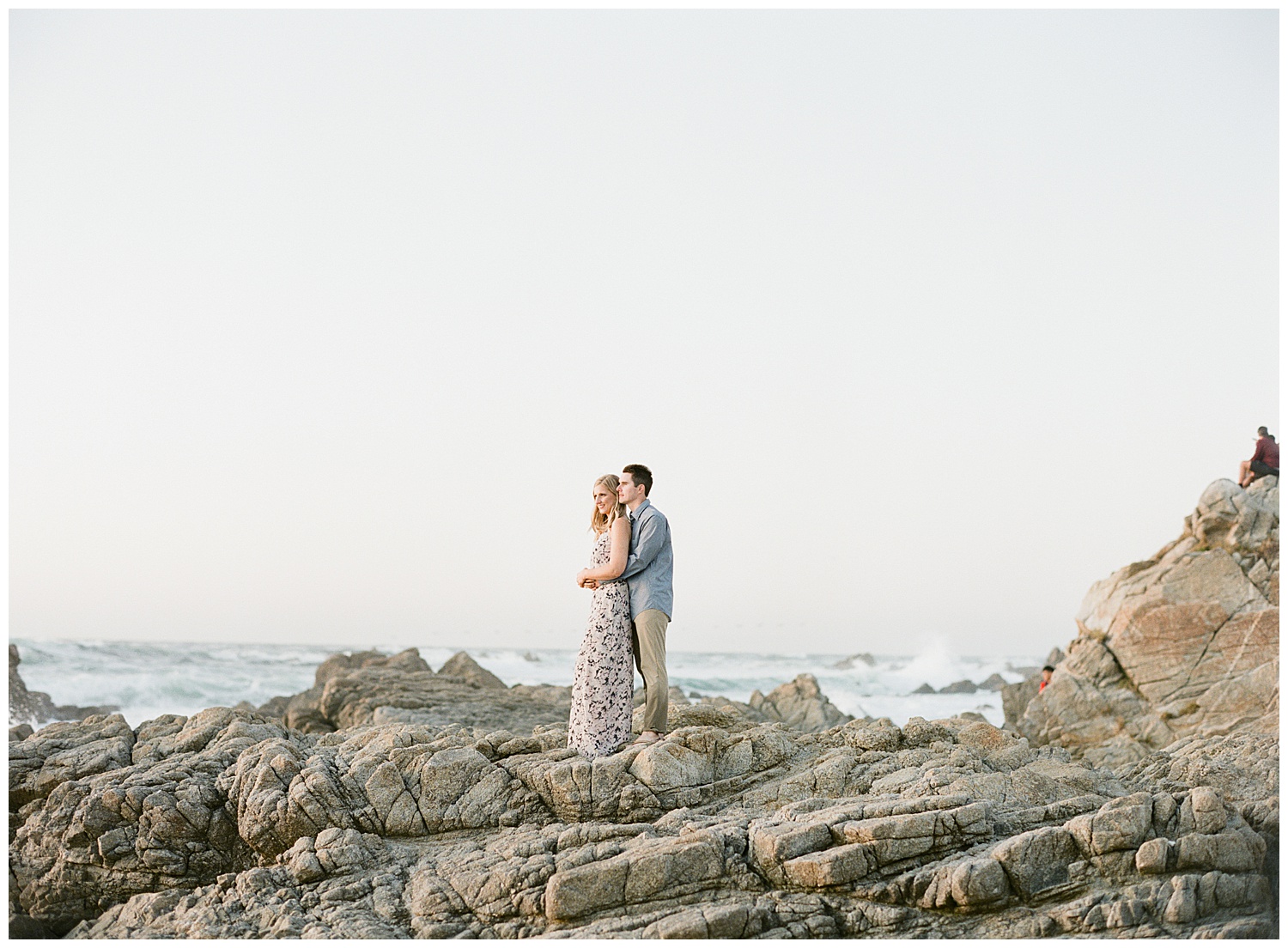 landscape photo of couple embracing on the rocks of Pebble Beach staring out at the ocean by film photographer Ags Photo Art