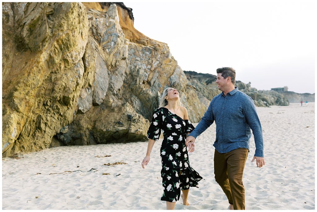 surprise engagement couple walking hand in hand happily on the sand at Garrapoda State Beach Park in Big Sur, CA by film photographer AGS Photo Art