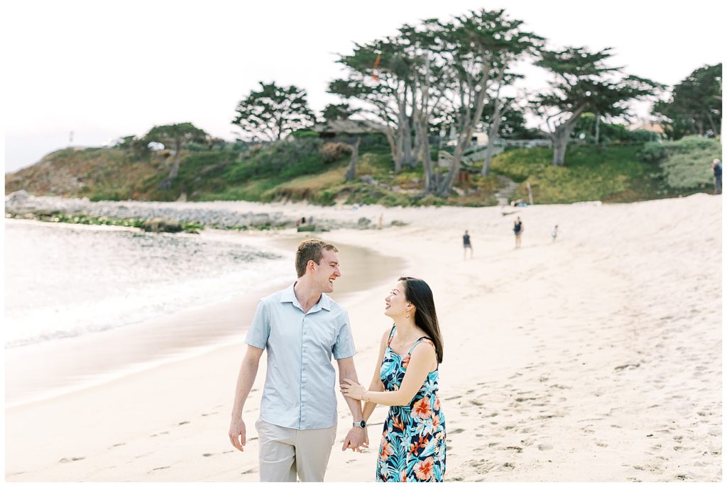 couple walking down the beach, hand in hand and smiling at each other