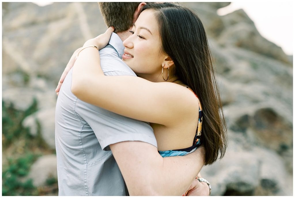 couple embracing each other in front of a tall rock structure