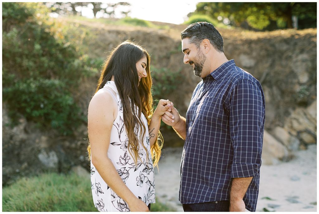 landscape couple's portrait of their Beautiful And Whimsical Monterey Surprise Proposal where they stare and smile at the woman's engagement ring