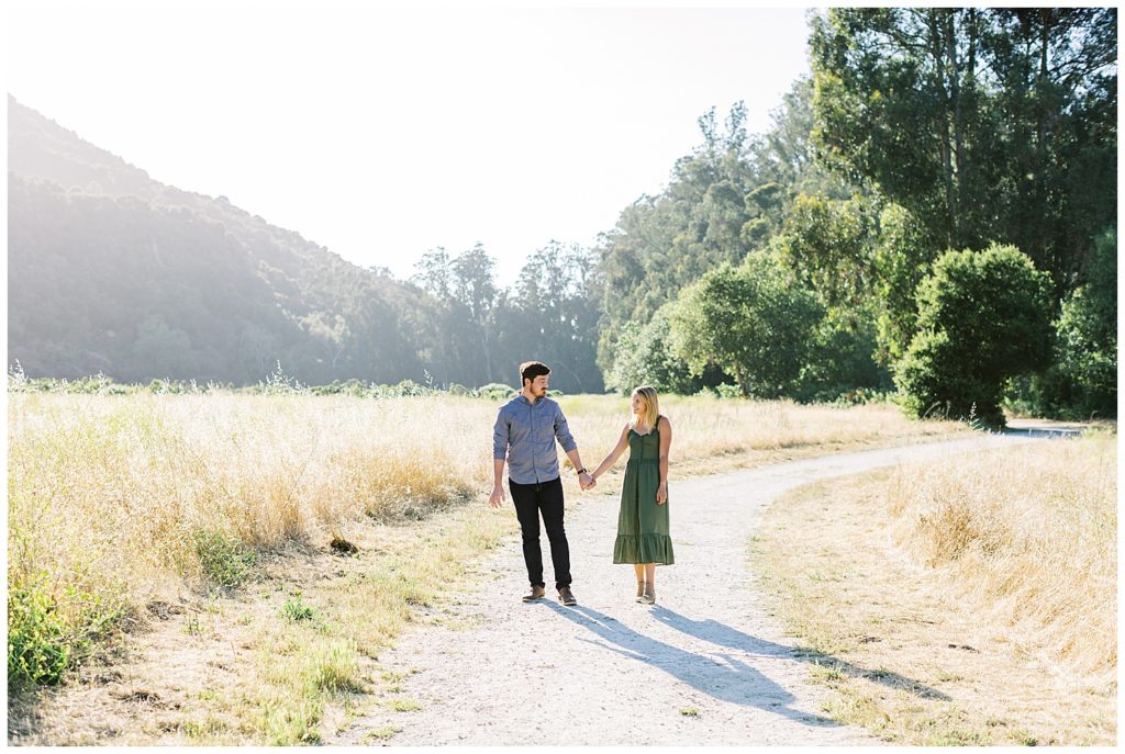 The couple hand in hand walking down an open path in a field