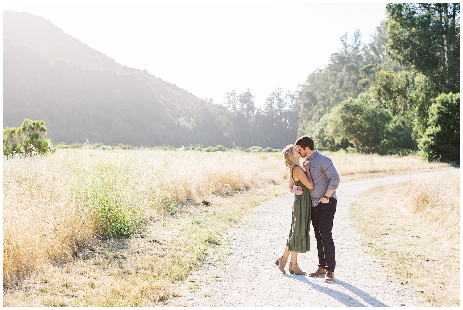 To celebrate their Powerful And Heartfelt Anniversary Session, the couple shares a sweet kiss in a golden field surrounded by trees and mountains by film photographer AGS Photo Art