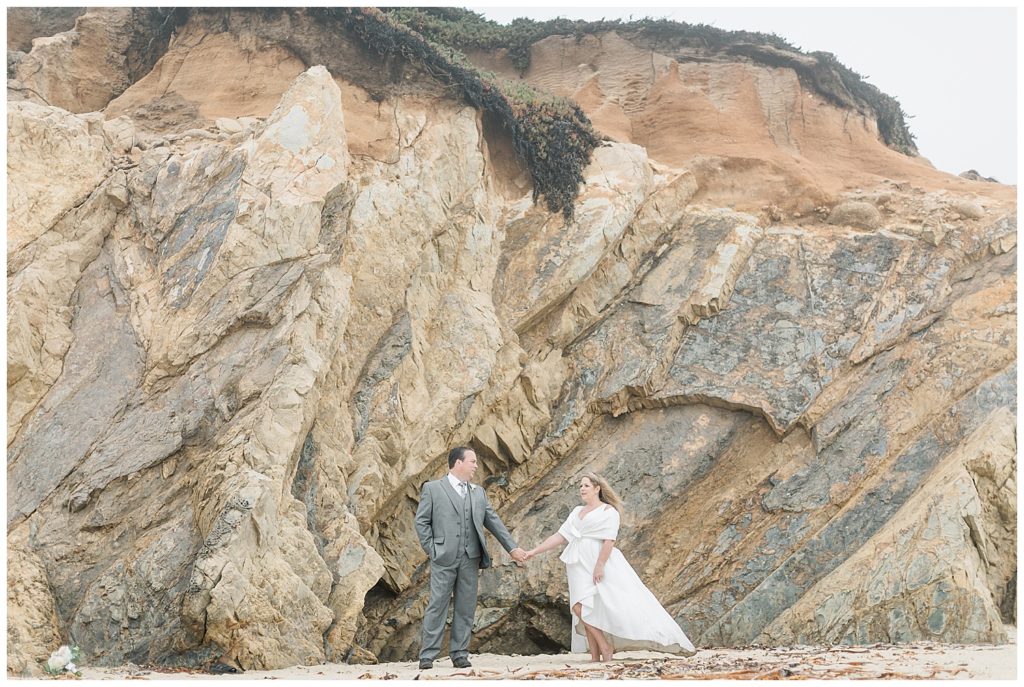elopement portrait of the bride and groom at the foot of a large mountain cliff on the beach of Big Sur, CA by film photographer AGS Photo Art