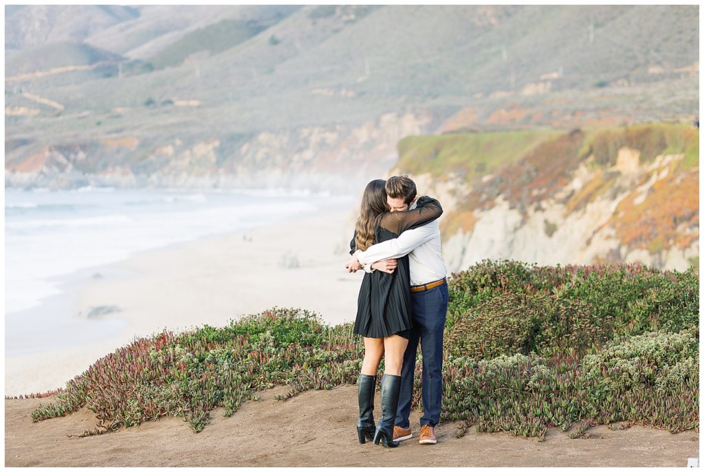 the couple hugging surrounded by greenery and beach waves on the cliffs of Big Sur CA