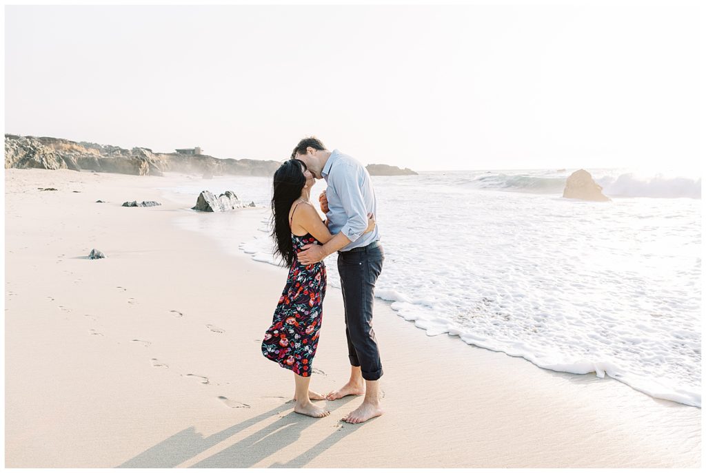 couple sharing a kiss on the shoreline at the beach in Big Sur while the foamy white waves wash in