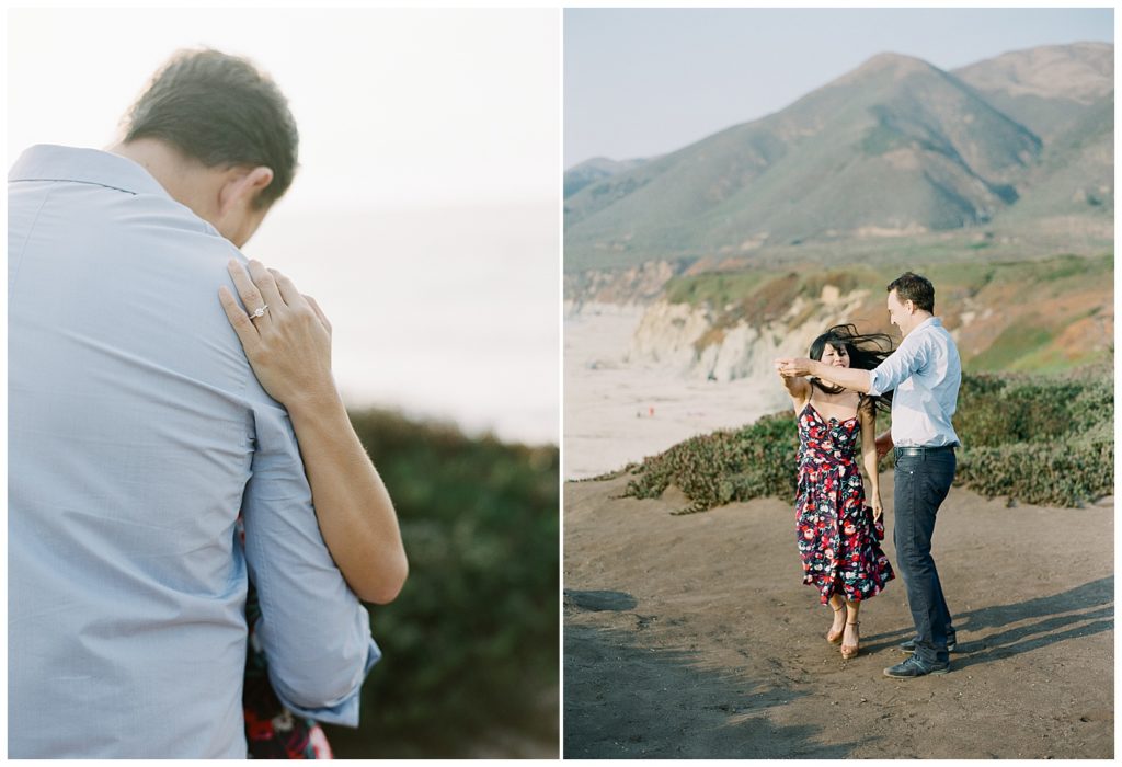 Big Sur Surprise Proposal couple portrait where the man's back is to the camera with the woman's hand on his shoulder, soft focus on her new engagement ring; windswept portrait of the couple on the cliffside