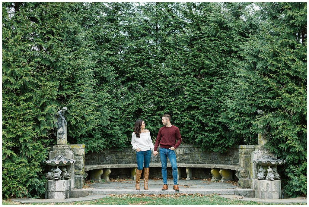 landscape photo of couple hand in hand and smiling at each other in front of a stone bench in New Jersey's Botanical Garden by film photographer AGS Photo Art