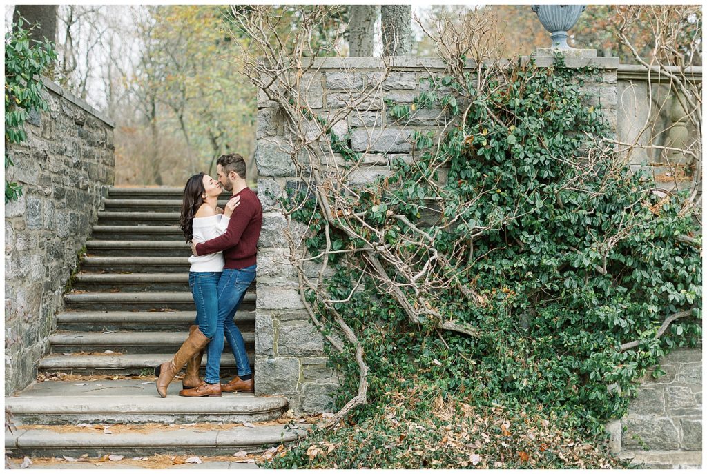 couple touching their noses together and leaning against a stone wall with green leaves and tree vines crawling up the side in New Jersey Botanical Garden by film photographer AGS Photo Art