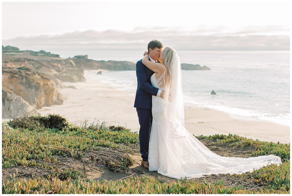 landscape photo of the bride and groom sharing a kiss on the cliffside at Pebble Beach with the waves and clouds rolling behind them by film photographer AGS Photo Art