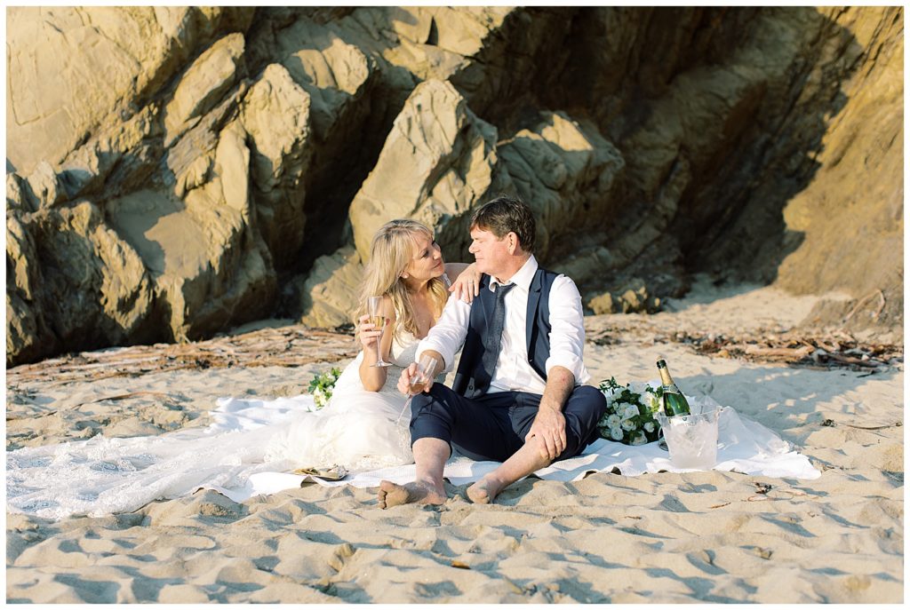 the couple enjoying champagne together during their picnic on the sand at Pebble Beach by film photographer AGS Photo Art
