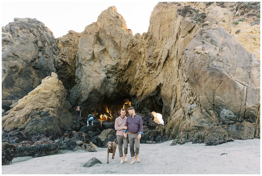 a brown labrador running happily around his two dads who just got engaged at Pfeiffer Beach by film photographer AGS Photo Art