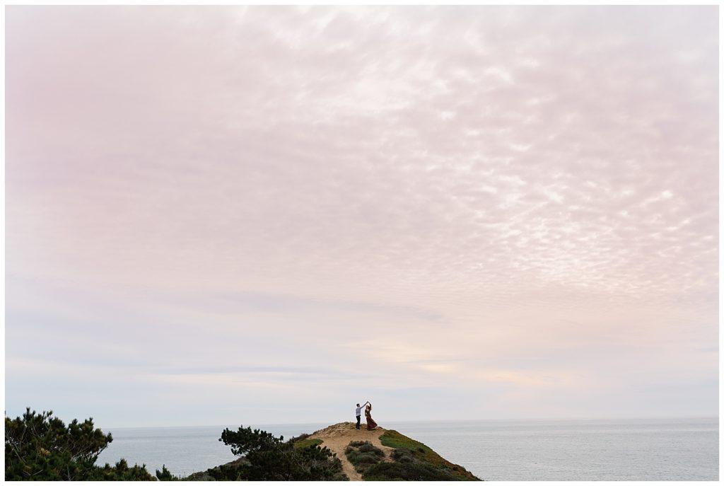 a far away landscape portrait of the man twirling his fiancée with a cotton candy sky overhead by film photographer AGS Photo Art