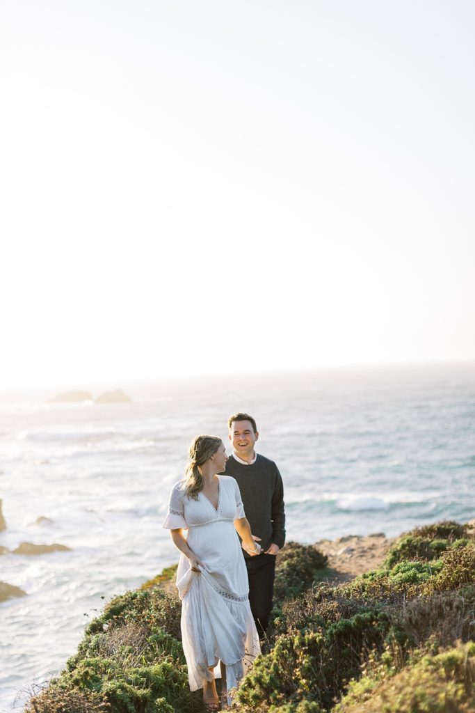 Big Sur coastline maternity session portrait of the couple walking towards the camera with the ocean behind them