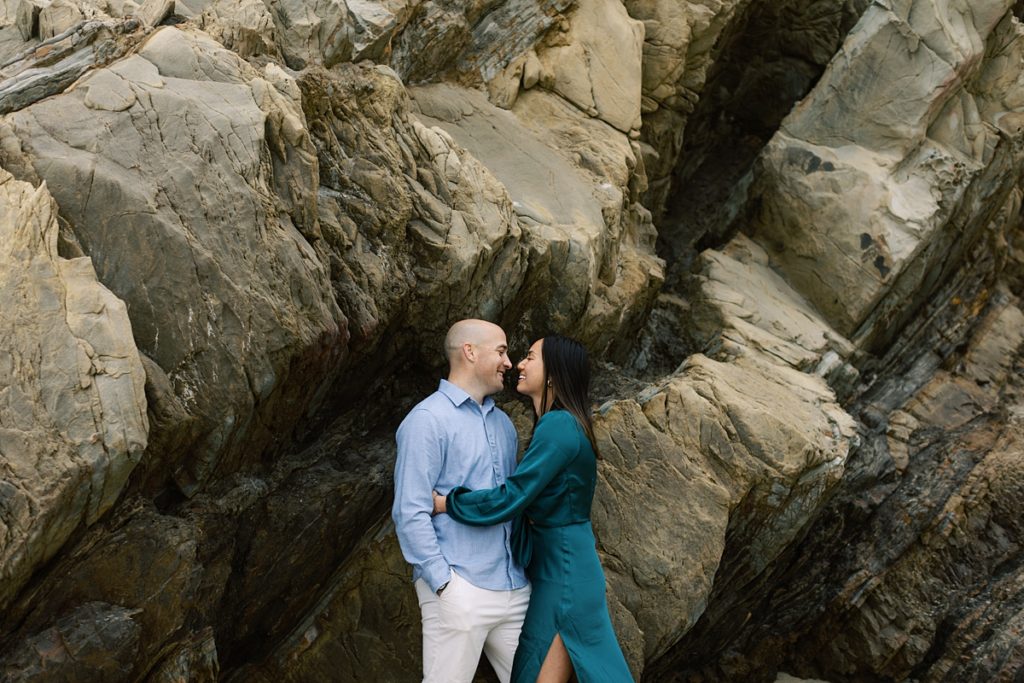 couple smiling at each other at the foot of cliffs in Big Sur