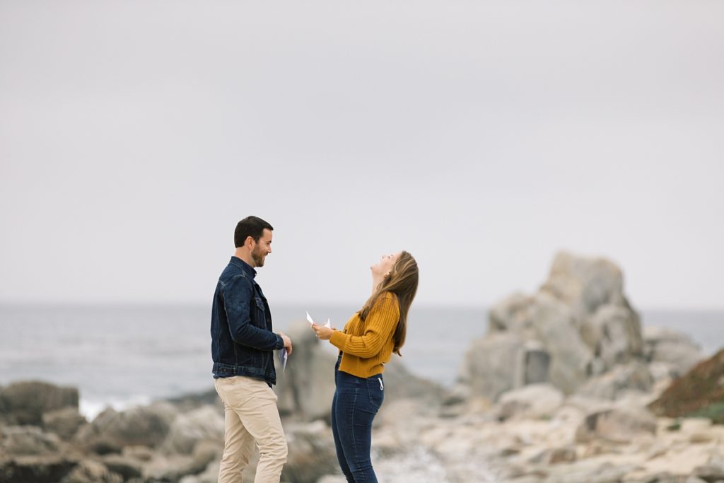 excited couple at Carmel Beach reading their weekend itinerary for how they're going to celebrate their proposal