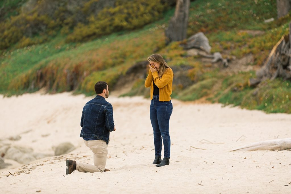 woman covering her face in surprise as her fiancé proposes to her at Carmel Beach by film photographer AGS Photo Art