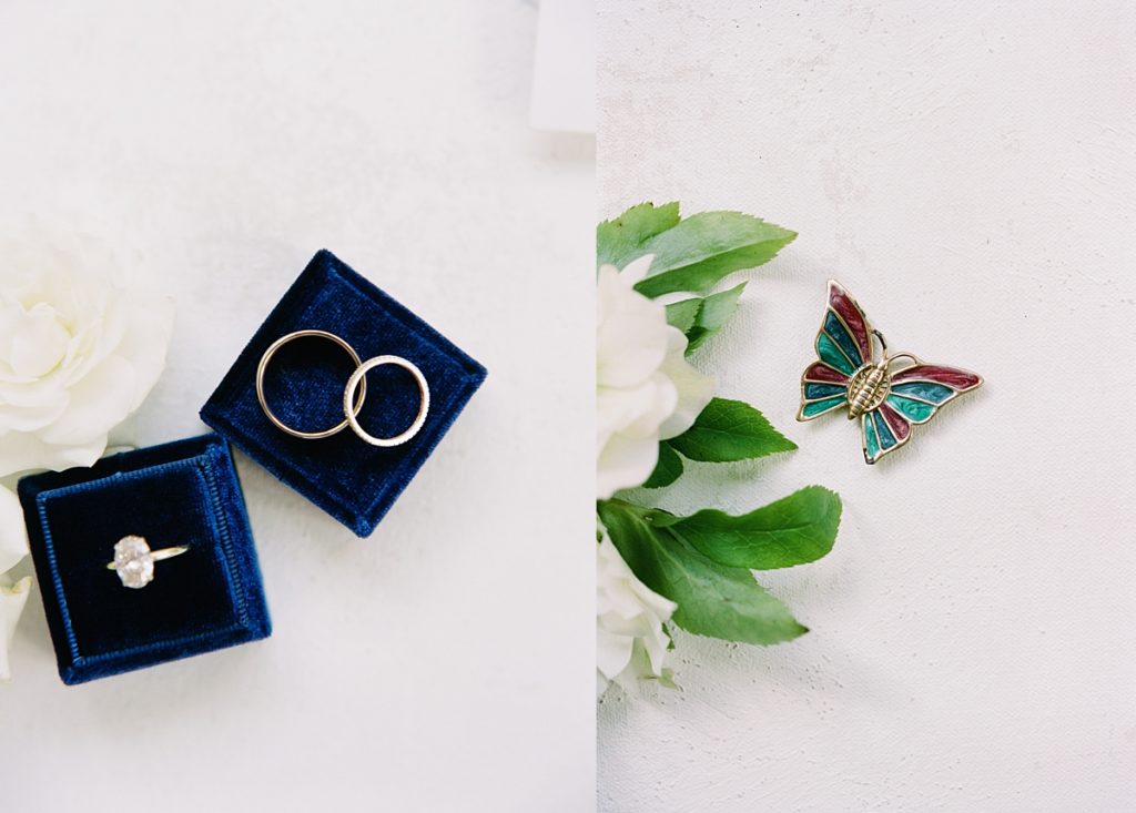 Pebble Beach intimate wedding day details: dark blue velvet ring box with his and her wedding rings and bangs; red, blue and green butterfly pin by film photographer AGS Photo Art