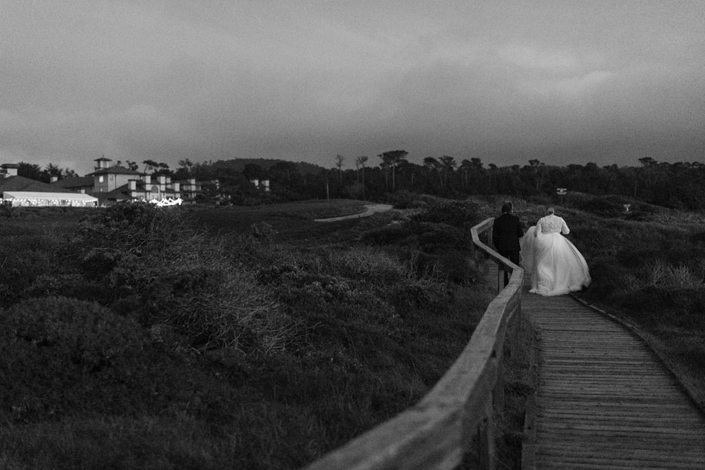 black and white Pebble Beach wedding photograph of couple walking up the wooden walkway back to The Inn At Spanish Bay