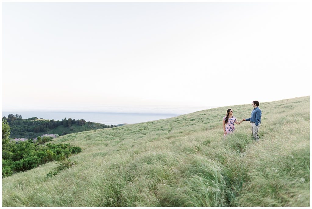 couple holding hands and facing each other on a grassy slope hill by film photographer AGS Photo Art