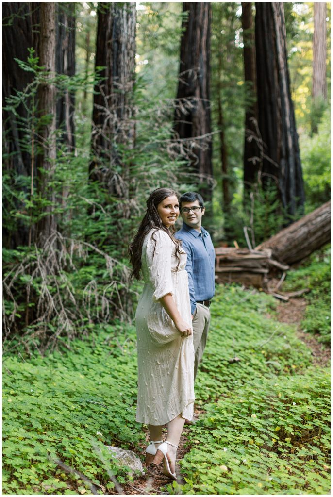 portrait of the couple in the forest with the woman looking over her shoulder and smiling at the camera