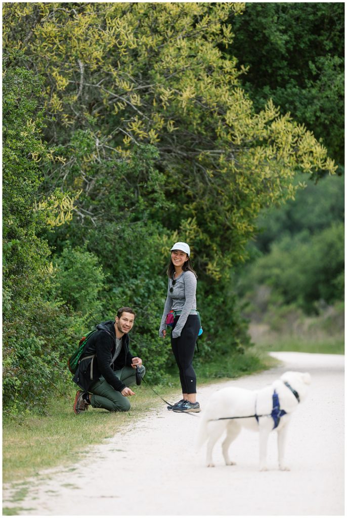 couple smiling at the camera and their dog on a hiking trail during their Carmel Valley Surprise Proposal by film photographer AGS Photo Art