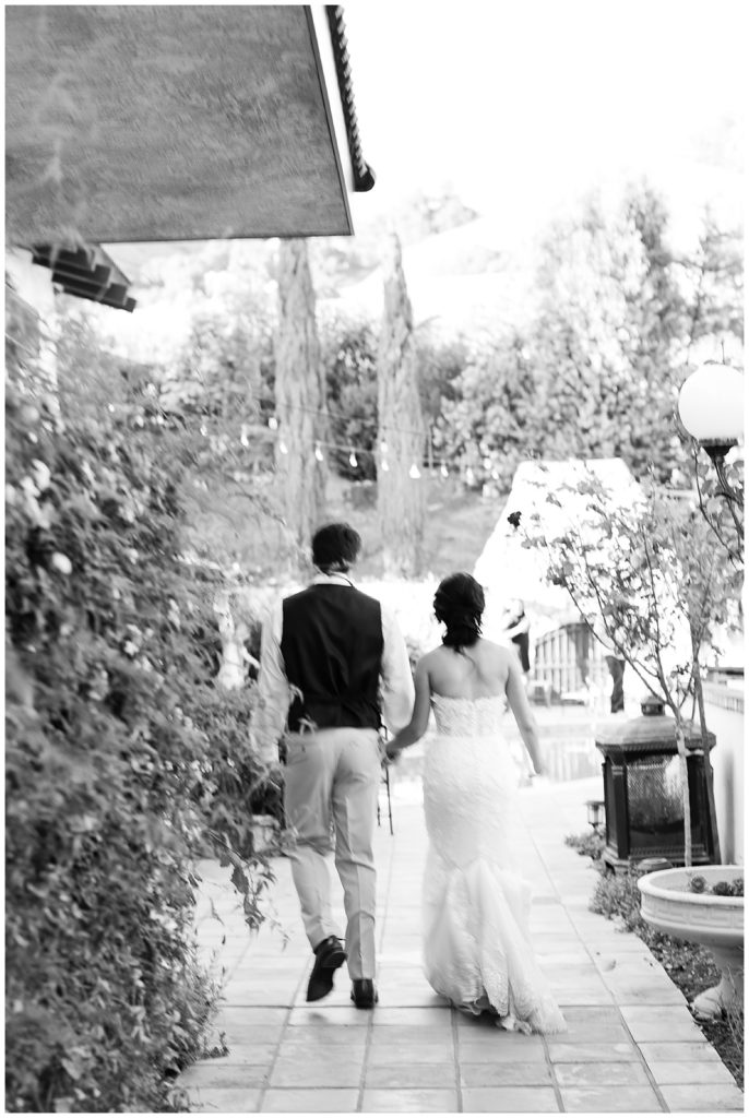 black and white Carmel Valley wedding portrait of the bride and groom hand in hand and walking away from the camera at Chateau Carmel by film photographer AGS Photo Art