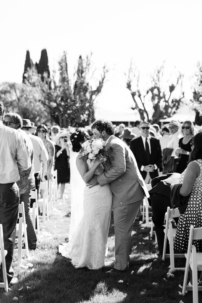 black and white portrait of the bride and groom sharing a kiss surrounded by their friends and family
