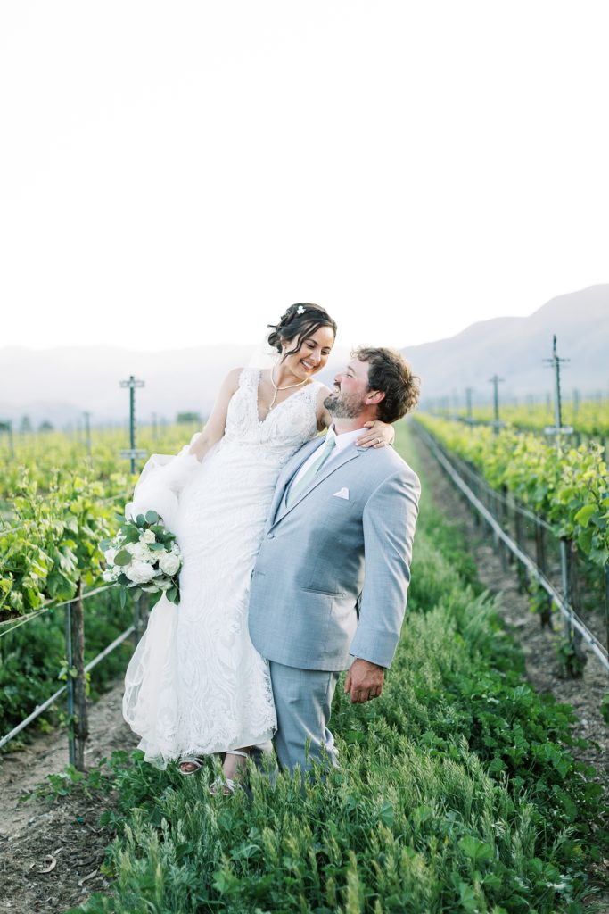 portrait of the groom holding up his bride while they're in the vineyards