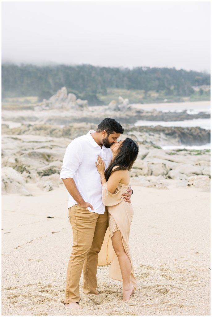 portrait of the couple sharing a kiss with Carmel by the Sea in the background