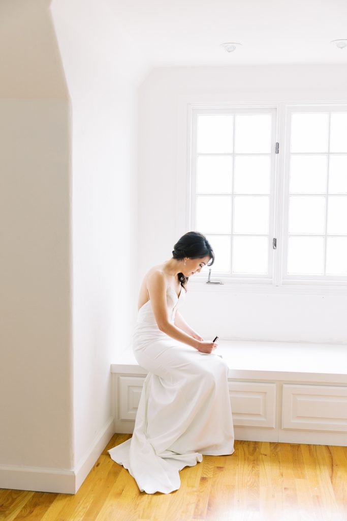 bride sitting by the window reading and writing her vows