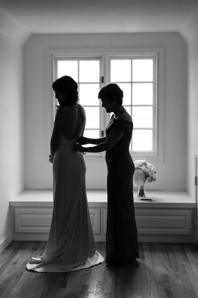black and white Luxury Carmel By The Sea Wedding photograph of the bride having her dress buttoned up by her mother in law