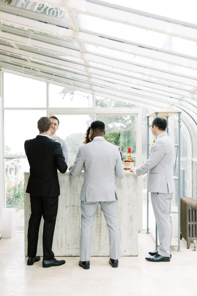 the groom and his groomsmen gathered around the bar in an indoor, glass patio