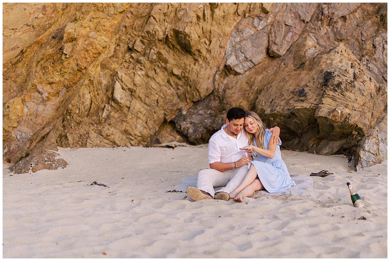 Carmel photographer portrait of couple at the beach looking at their ring with champagne and a blanket