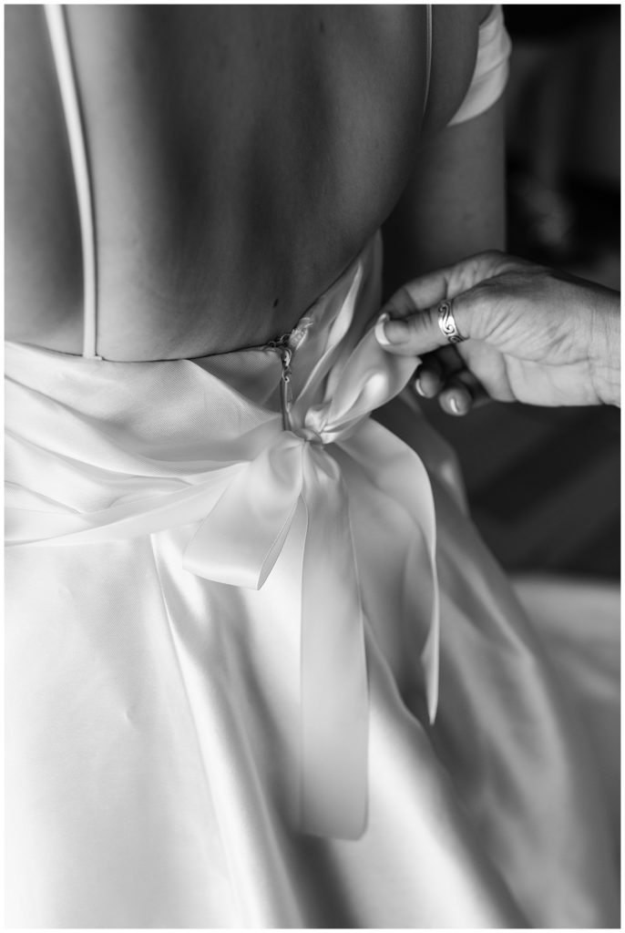 black and white photo of the back of the bride's dress where a hand is tying a ribbon