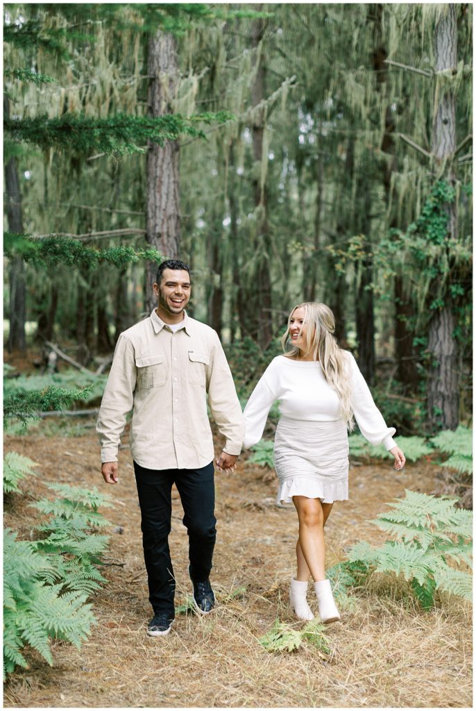 Pebble Beach engagement session in the forest with the couple walking hand in hand towards the camera
